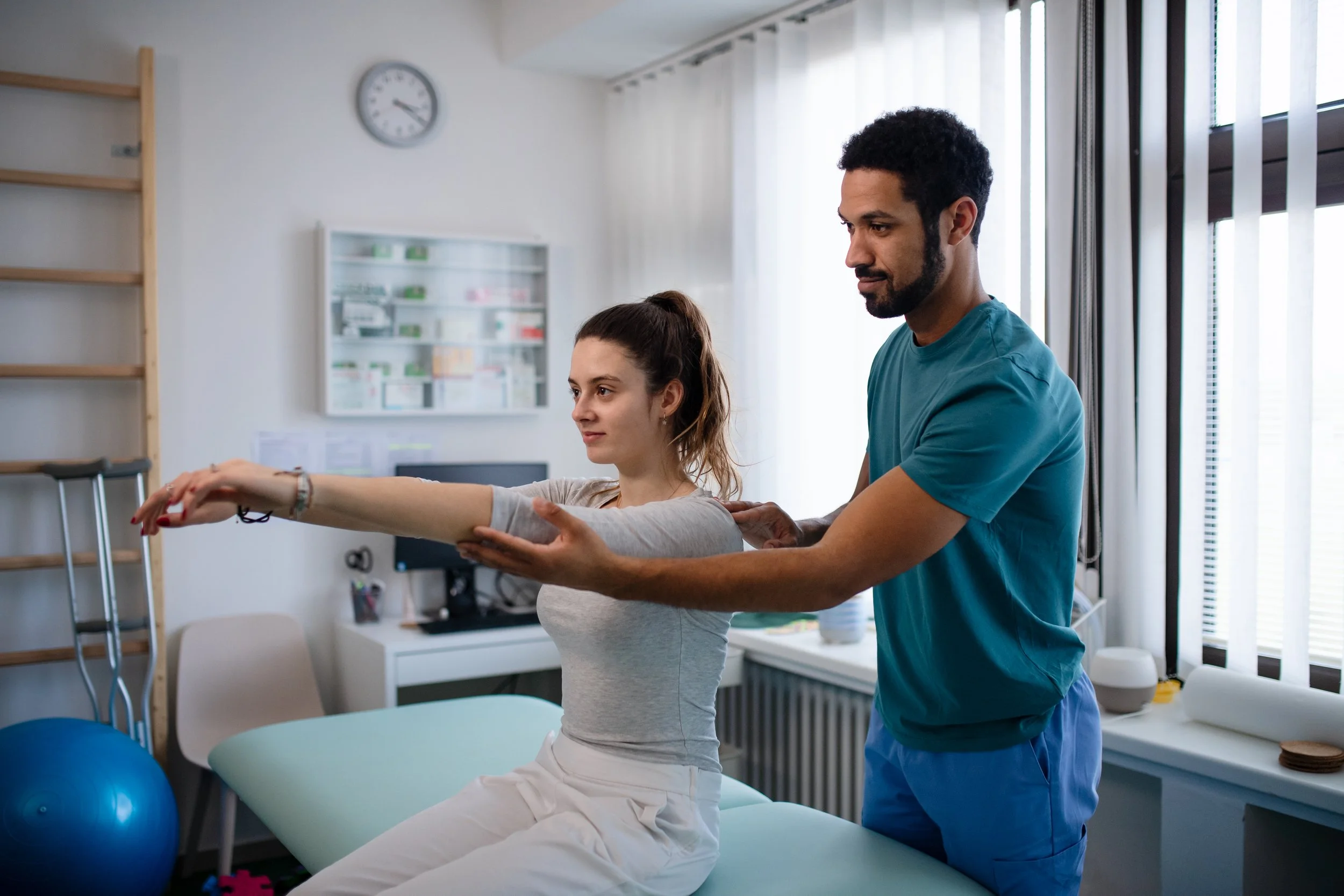 Physical therapist assisting a woman with arm exercises in a clinic.