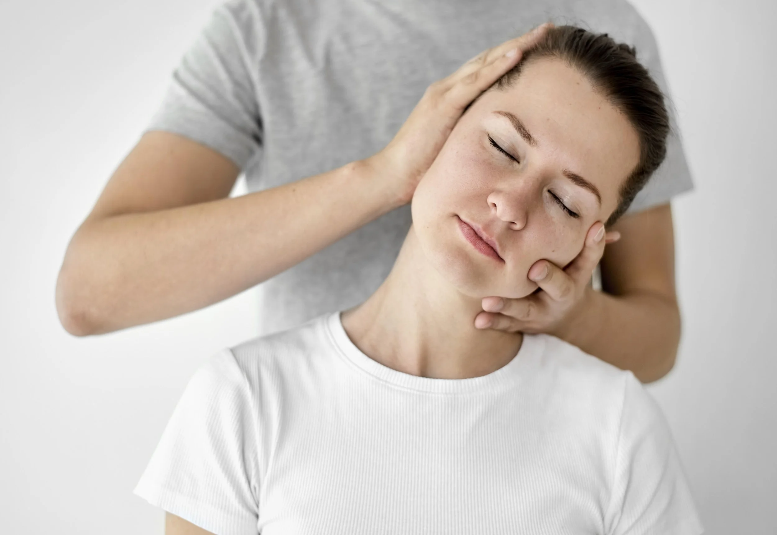 Person receiving a gentle head massage, wearing a white shirt, looking relaxed.