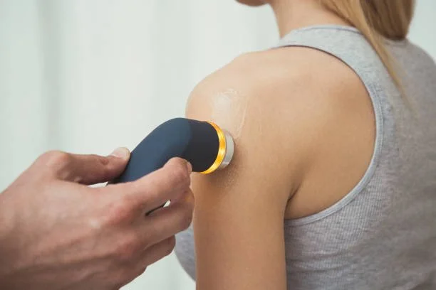 Close-up of a person receiving shoulder treatment with a handheld device in a medical or therapeutic setting.